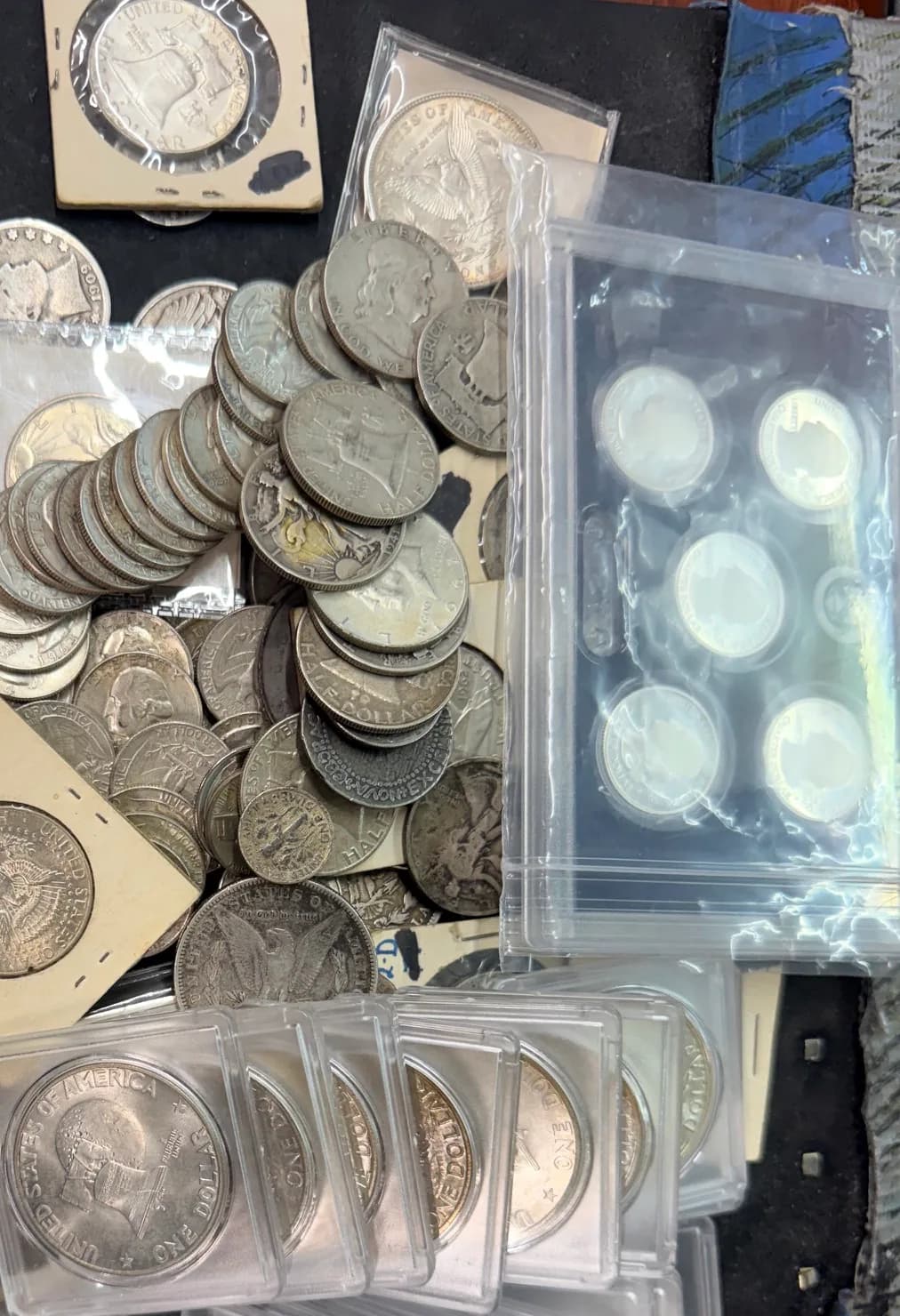A mixed lot of 90% silver halves, quarters, and dimes in flips and tubes next to a proof set and slabbed silver dollars